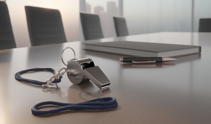 Closeup of a silver coaching whistle sitting on a board table next to a notebook and pen in and empty boardroom
